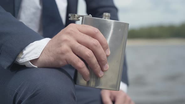 Close-up of Male Hand Holding Flask with Alcohol Outdoors. Unrecognizable Caucasian Businessman in alt