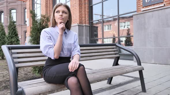Pensive Woman Thinking and Sitting Outside Office Building on Bench alt