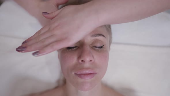 Closeup Relaxed Woman with Closed Eyes Lying in Spa Salon with Hands Massaging Forehead in Slow alt