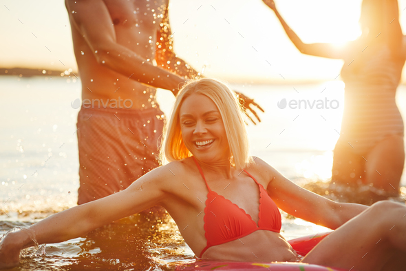 Smiling young woman and friends splashing water in a lake - Stock Photo - Images