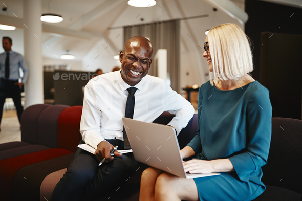 Two coworkers laughing together while sitting on an office soafa - Stock Photo - Images