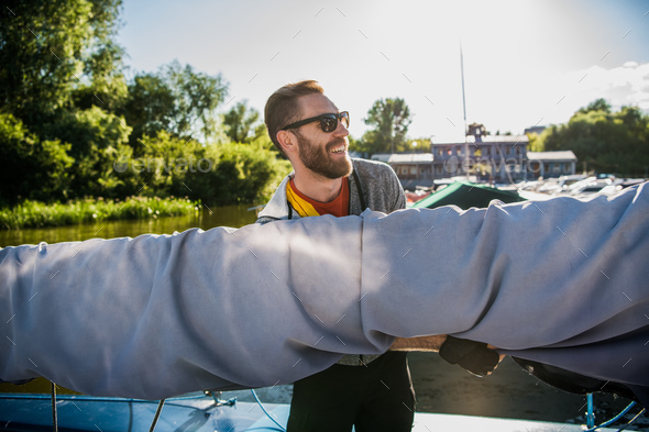 Young sailor in sunglasses holds and moves main sail with both hands. He is happy and smiling. Young - Stock Photo - Images