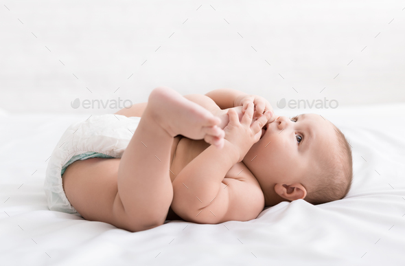 Adorable little baby sucking foot lying on bed