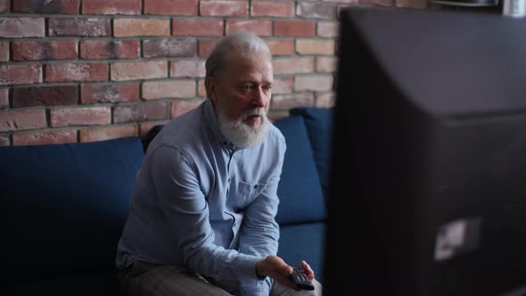 Excited Disappointed Grayhaired Senior Man Fan Sitting at TV Screen on Sofa at Home and Watching alt