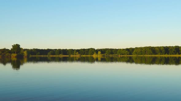 Panorama of a Large Lake with Quiet Water, Forest on the Opposite Bank Under a Blue Sky in the alt