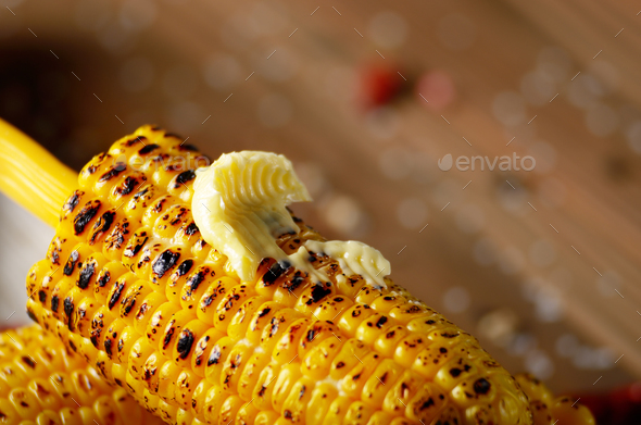 Deep grilled sweet corn cob under melting butter on plastic hold