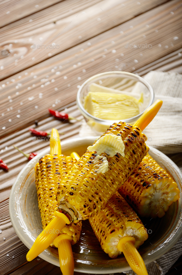Wooden table with deep grilled sweet corn cobs under melting but