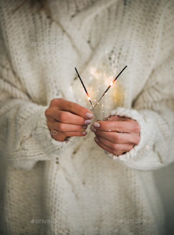 Woman in sweater holding Christmas sparklers in hands, close-up - Stock Photo - Images