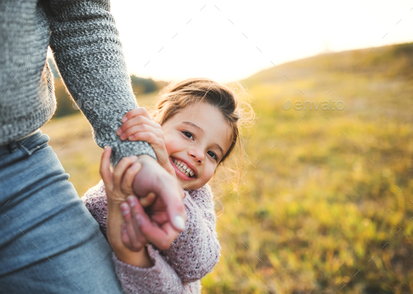 A small girl with unrecognizable father in autumn nature, having fun.