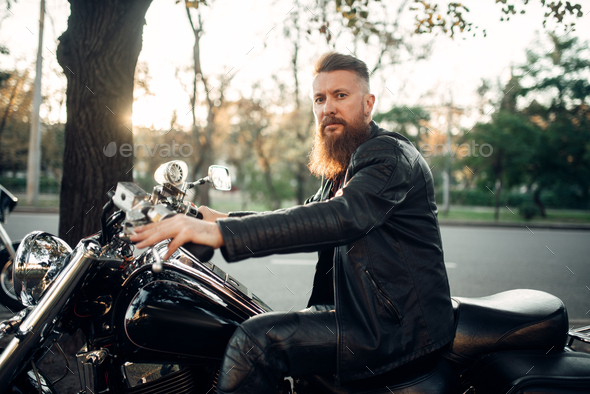 Baerded biker poses on chopper leaning on a helmet Stock Photo by ...