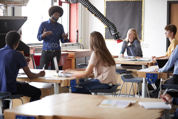 Class Of High School Students Sitting At Work Benches Listening To