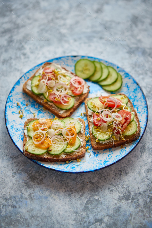 Plate with toasts with cucomber, tomatoes and crumbled feta and radish sprouts