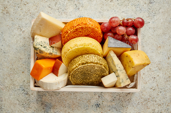 Fresh and delicious different kinds of cheeses placed in wooden crate with grapes - Stock Photo - Images