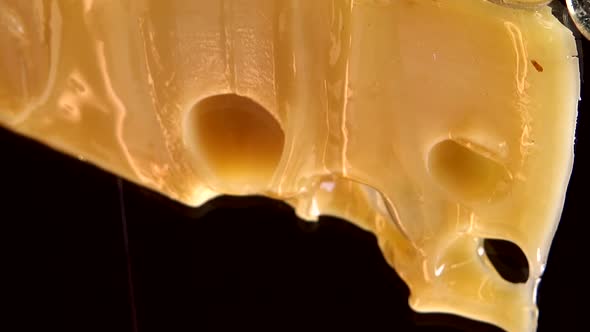 Drops of honey flow down from the cheese on a mirrored black background. alt