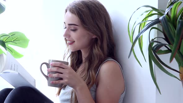 Happy Young Woman Reading Book And Drink Cup Of Coffee At Morning