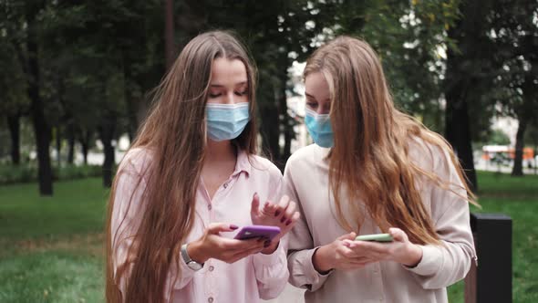 Couple of Tourists or Girls Student Walking in a City Street in Medical Face Masks Use Smartphones alt