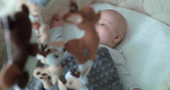 Cute Baby Boy Lying in Bed with Moving Toys and Rejoicing alt