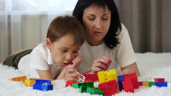 Happy Family Resting Lying on the Bed. Mother and Child Play, Building of Colored Blocks alt