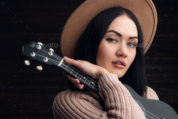 Close up portrait of young caucasian woman playing ukulele in front of a wooden background. Studio - Stock Photo - Images