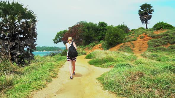 travel on a tropical island, girl tourist walking along a trail past palm trees overlooking the sea alt