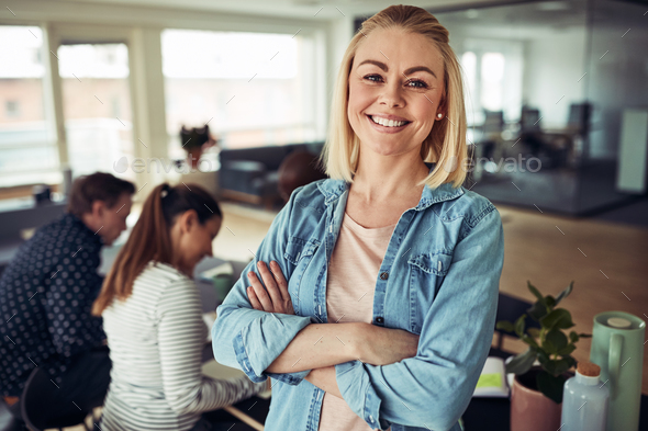Smiling young businesswoman with colleagues working in the background - Stock Photo - Images