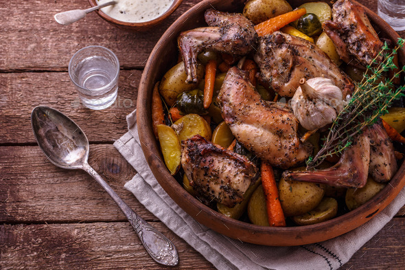 Oven baked rabbit with root vegetables and herbs, rustic style
