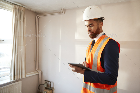 Surveyor In Hard Hat And High Visibility Jacket With Digital Tablet Carrying Out House Inspection
