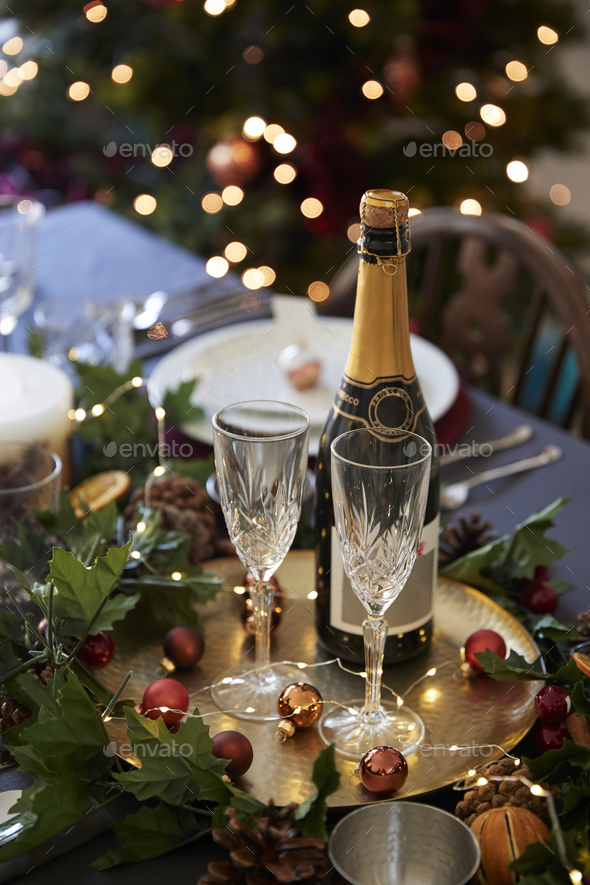 Christmas table setting with glasses and a bottle of champagne, baubles arranged on a gold plate - Stock Photo - Images