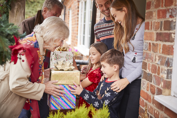 Grandparents Being Greeted By Family As They Arrive For Visit On Christmas Day With Gifts