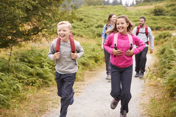 Close up of children running ahead of parents on a country path during a family vacation, front view