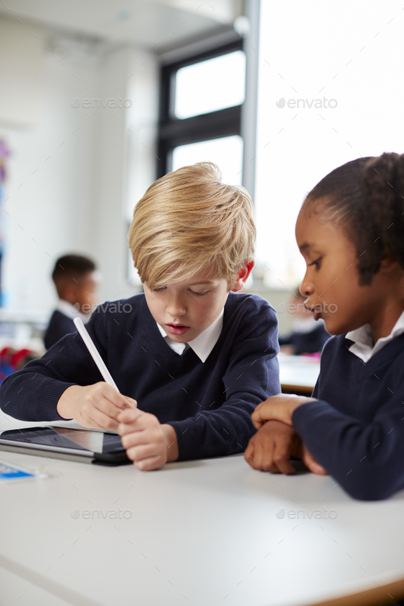 Two Primary School Kids Using A Tablet Computer And Stylus Sitting