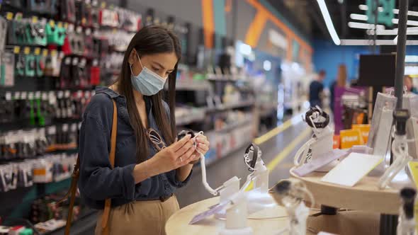 Female Customer Wearing Face Protective Mask Looking at New Model of Smartwatch at Shop alt