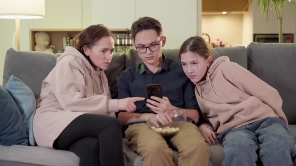 Happy Family Mother with Adult Son and Daughter Sitting on the Sofa in the Living Room Hugging While alt
