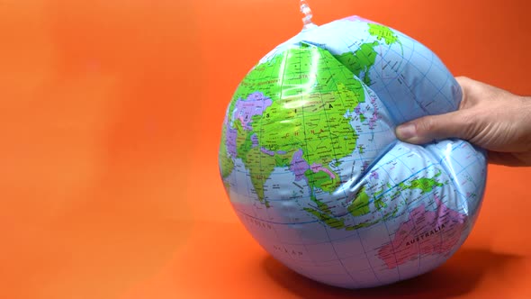 Hand Tightly Gripping an Earth Globe on Orange Background