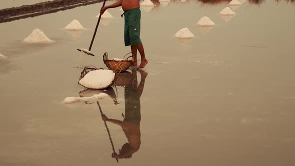 Low section shot of a salt field worker harvesting salt in Kampot, Cambodia alt
