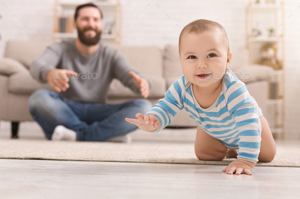 Adorable baby boy crawling on floor with dad Stock Photo by Prostock-studio