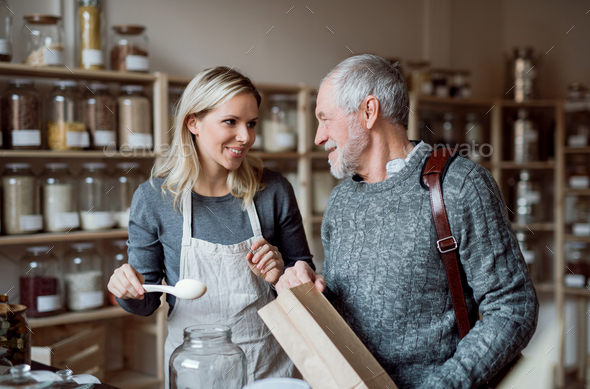 Young female shop assistant serving a senior man in a zero waste shop.