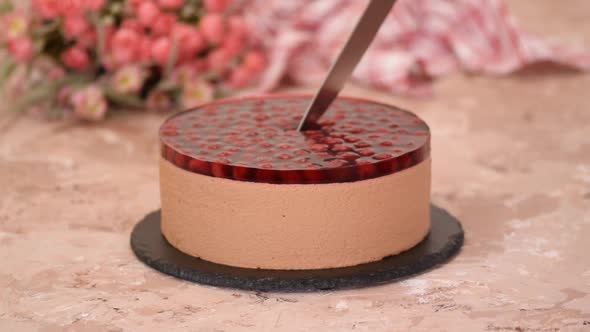 Cutting chocolate mousse cake with cherries jelly.