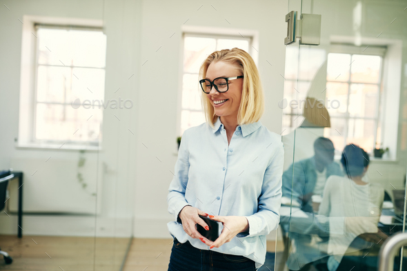 Laughing businesswoman standing with her cellphone in a modern office - Stock Photo - Images