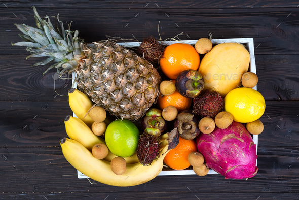 Fresh exotic fruits in a wooden box, top view with many colorful ripe fruits