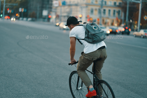 Young modern man cycling on a classic bike on the city road with a backpack