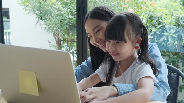 Young asian mother enjoy teaching her adorable daughter listen a music on a laptop.