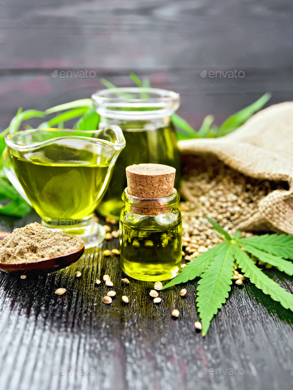 Oil hemp in two jars and sauceboat on dark board - Stock Photo - Images