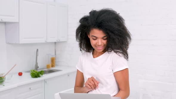 Woman in the kitchen. Holding laptop.