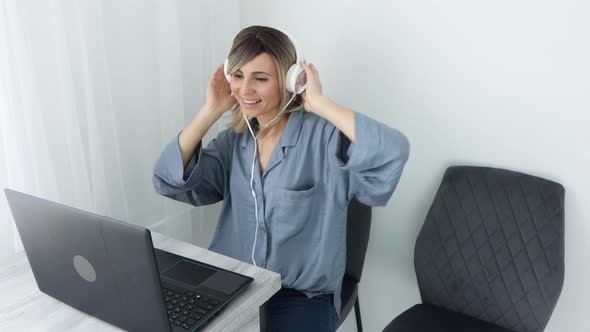 Attractive european blonde woman in headphones listening music and dancing sitting on comfy chair