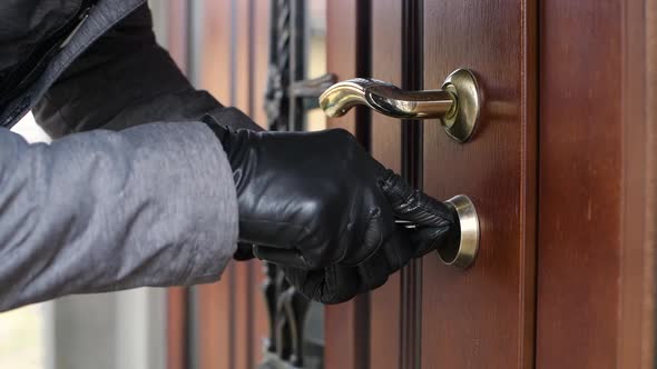 a thief in gloves opens the door lock of a private house and penetrates inside alt