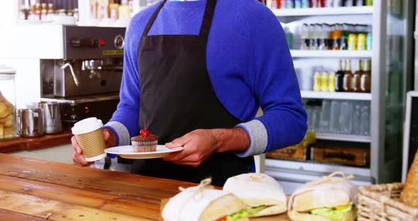 Waiter serving coffee and cupcake to customer at counter alt
