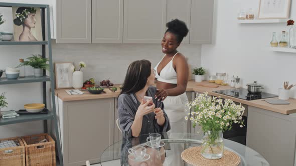 Affectionate Woman Pouring Coffee for Girlfriend in Kitchen alt