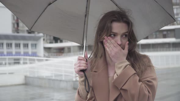 Young Ill Caucasian Woman Couching As Standing Outdoors Under Rain and Waiting. Portrait of Brunette alt