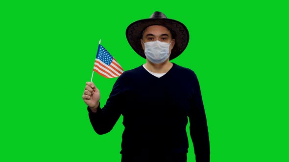 Adult Man in Protective Mask and Cowboy Hat Walking with Waving Flag of USA 